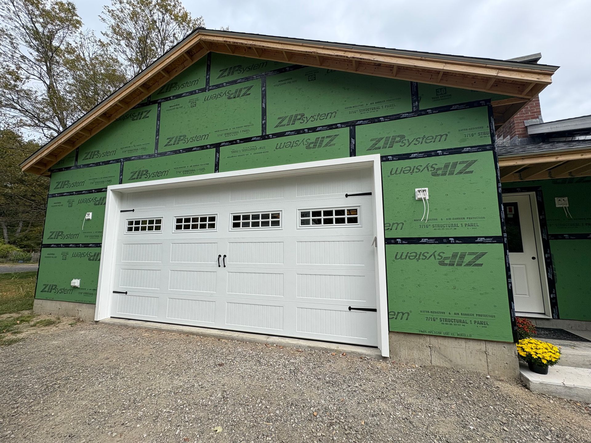 White garage door on a house under construction; green sheathing visible.