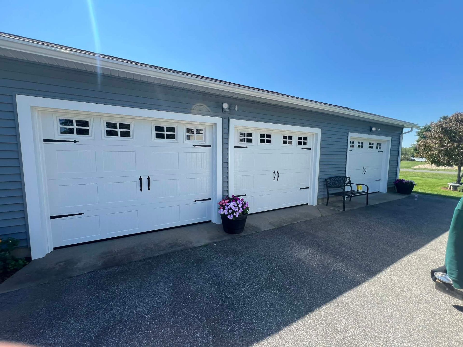 Two white garage doors with black hardware on a blue-sided building with a paved driveway.