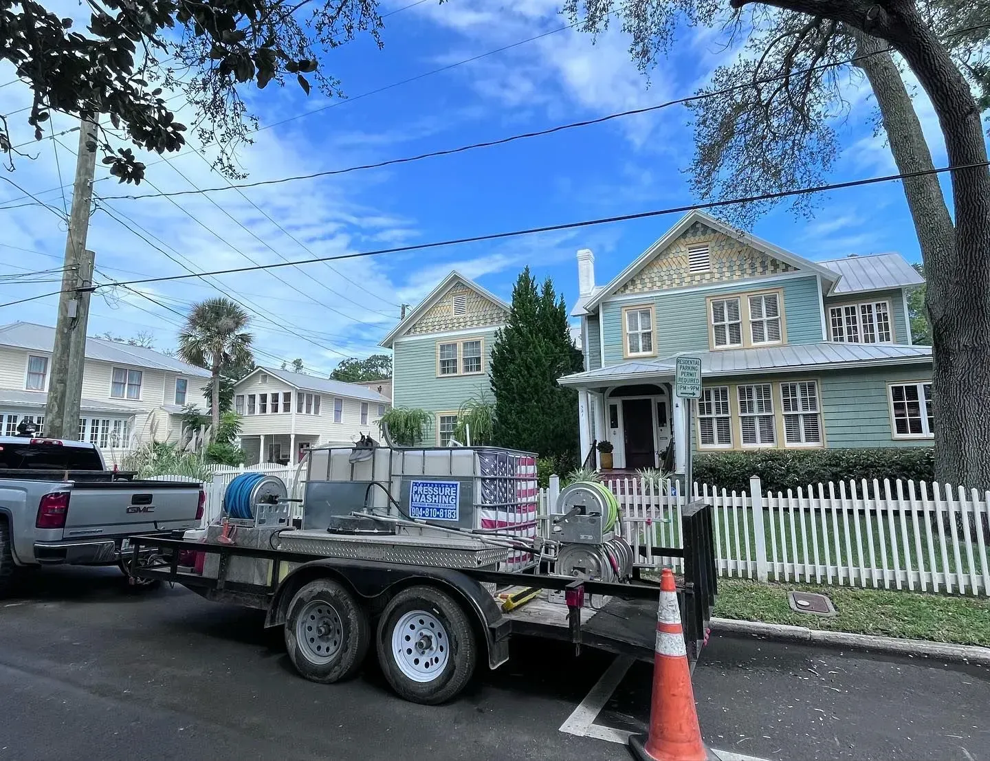 A trailer and truck parked in front of a blue-green house with a white picket fence.