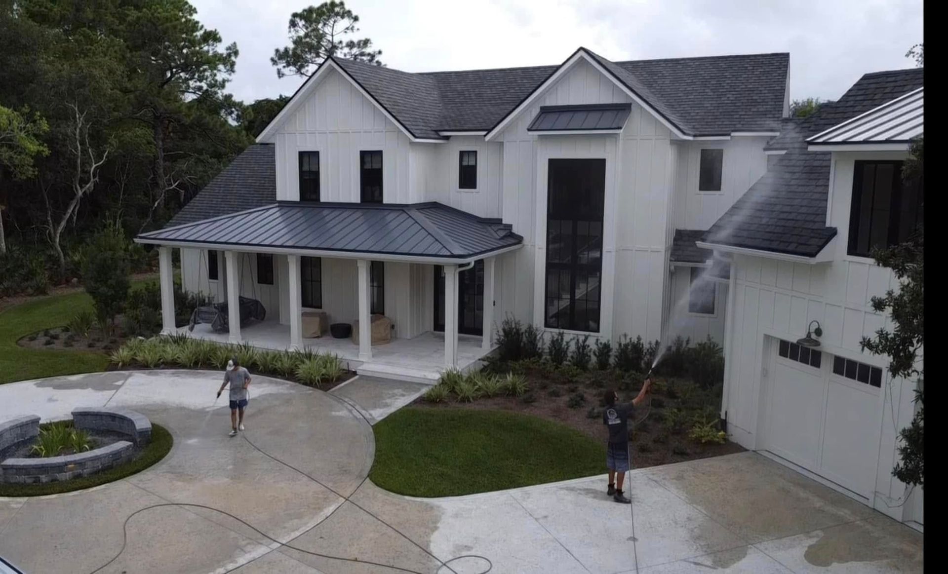 Man in front of a blue house with a book and plants. Sunny day, green grass, light blue shirt, white hat.