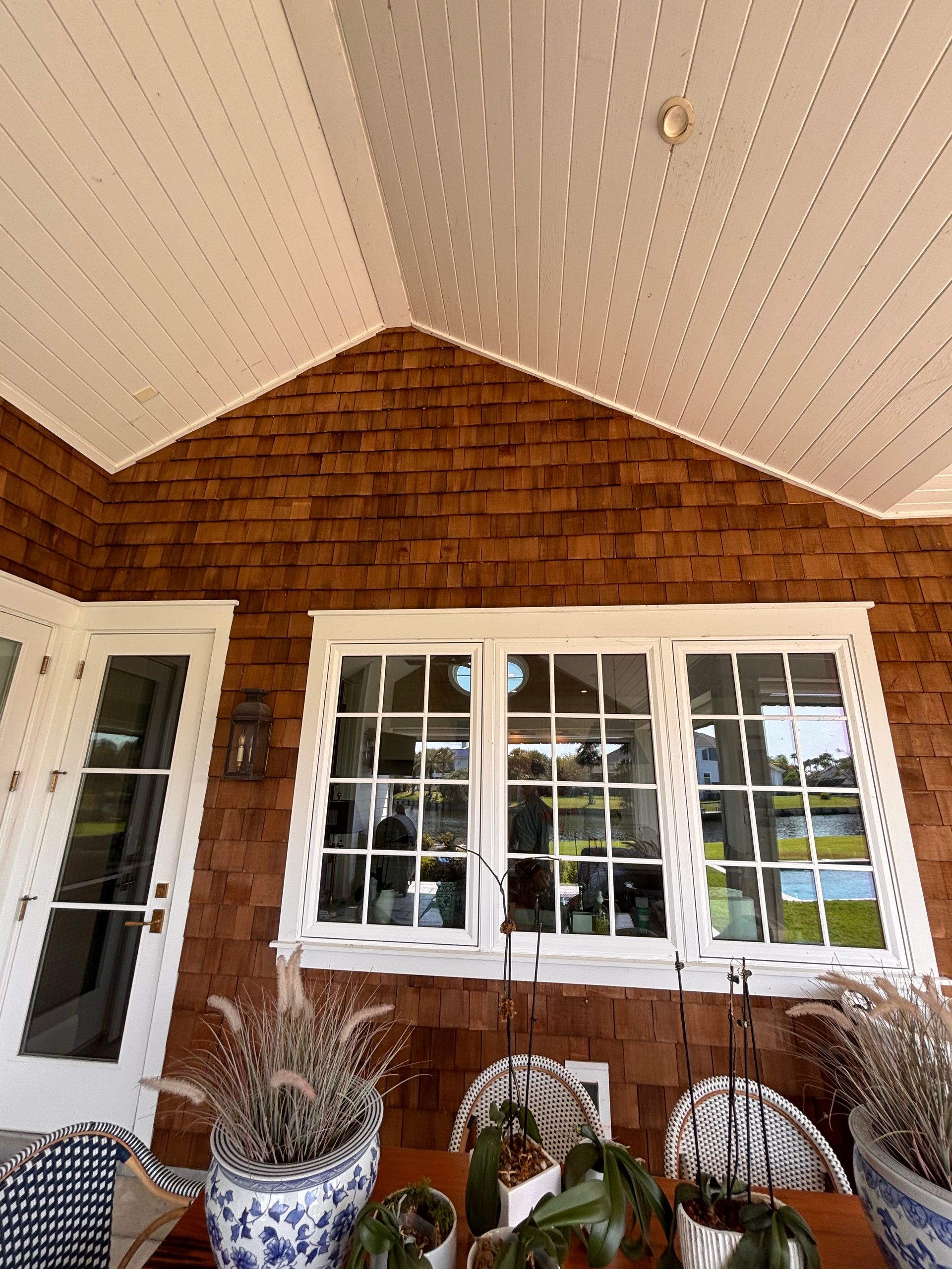 Person on tall ladder washing windows of a two-story tan house with blue accents.