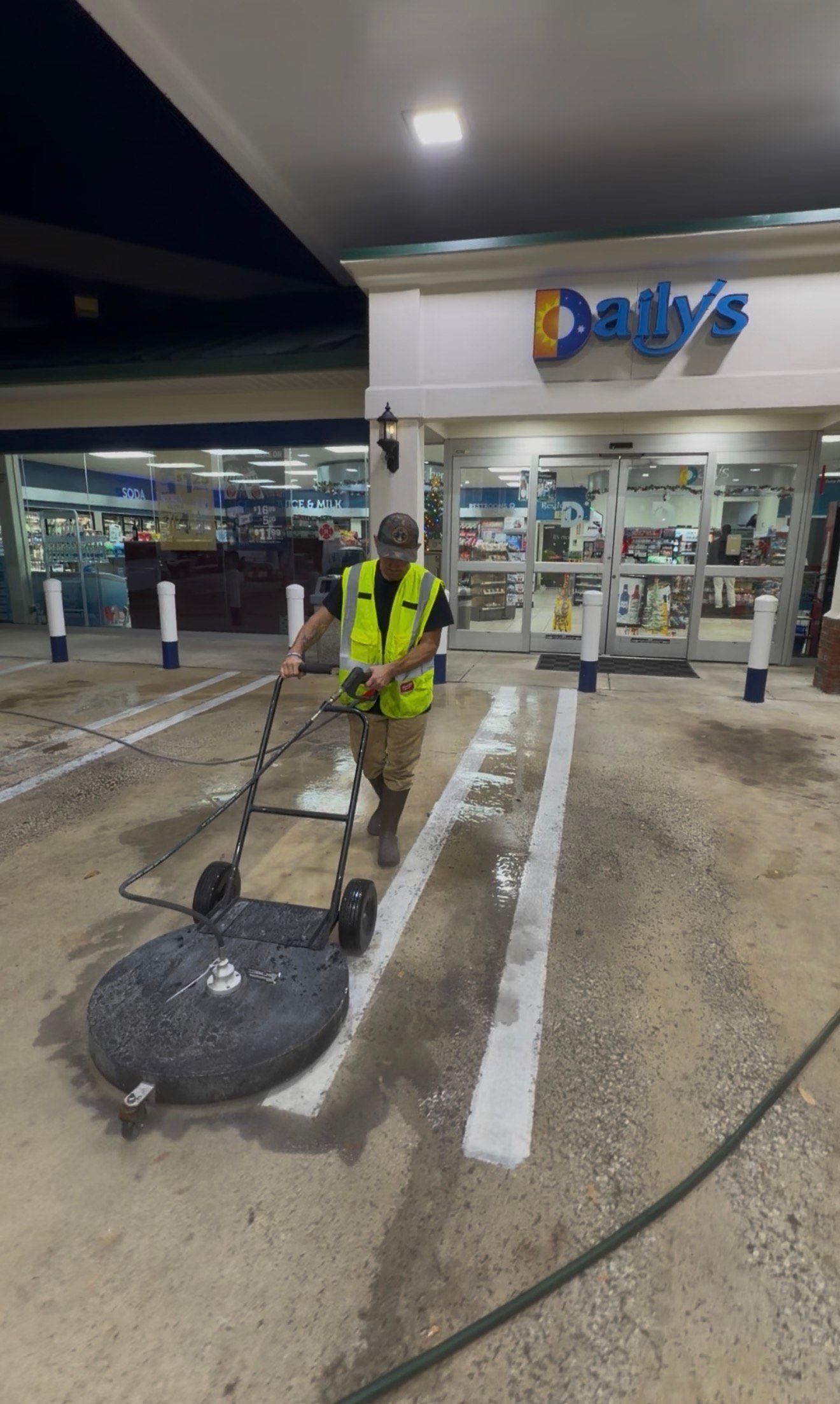 A person in a safety vest using a surface cleaner to clean a gas station forecourt.