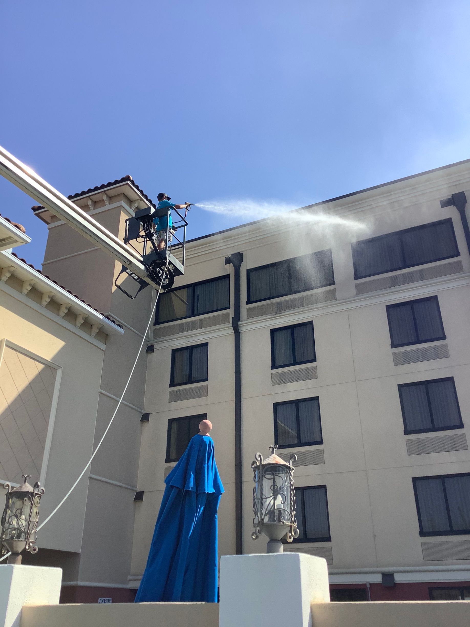 Man in lift spraying water on building exterior.