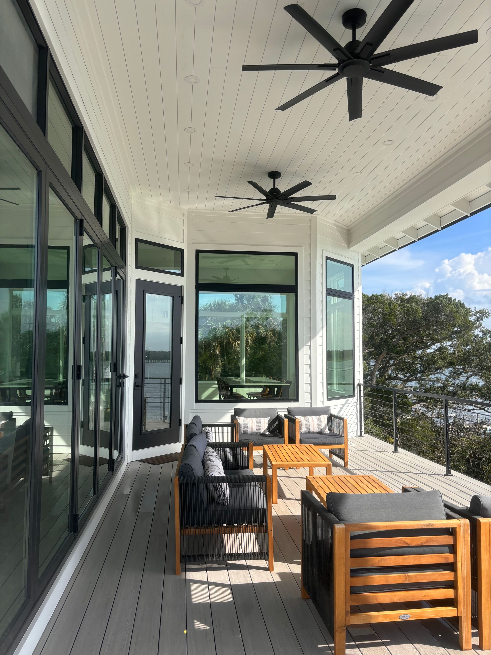 Person on tall ladder washing windows of a two-story tan house with blue accents.