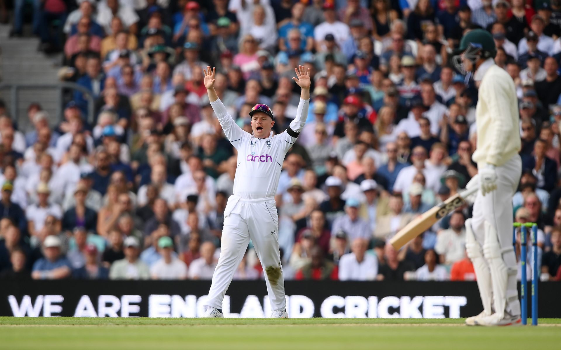 A cricket player is standing on a field with his arms in the air.