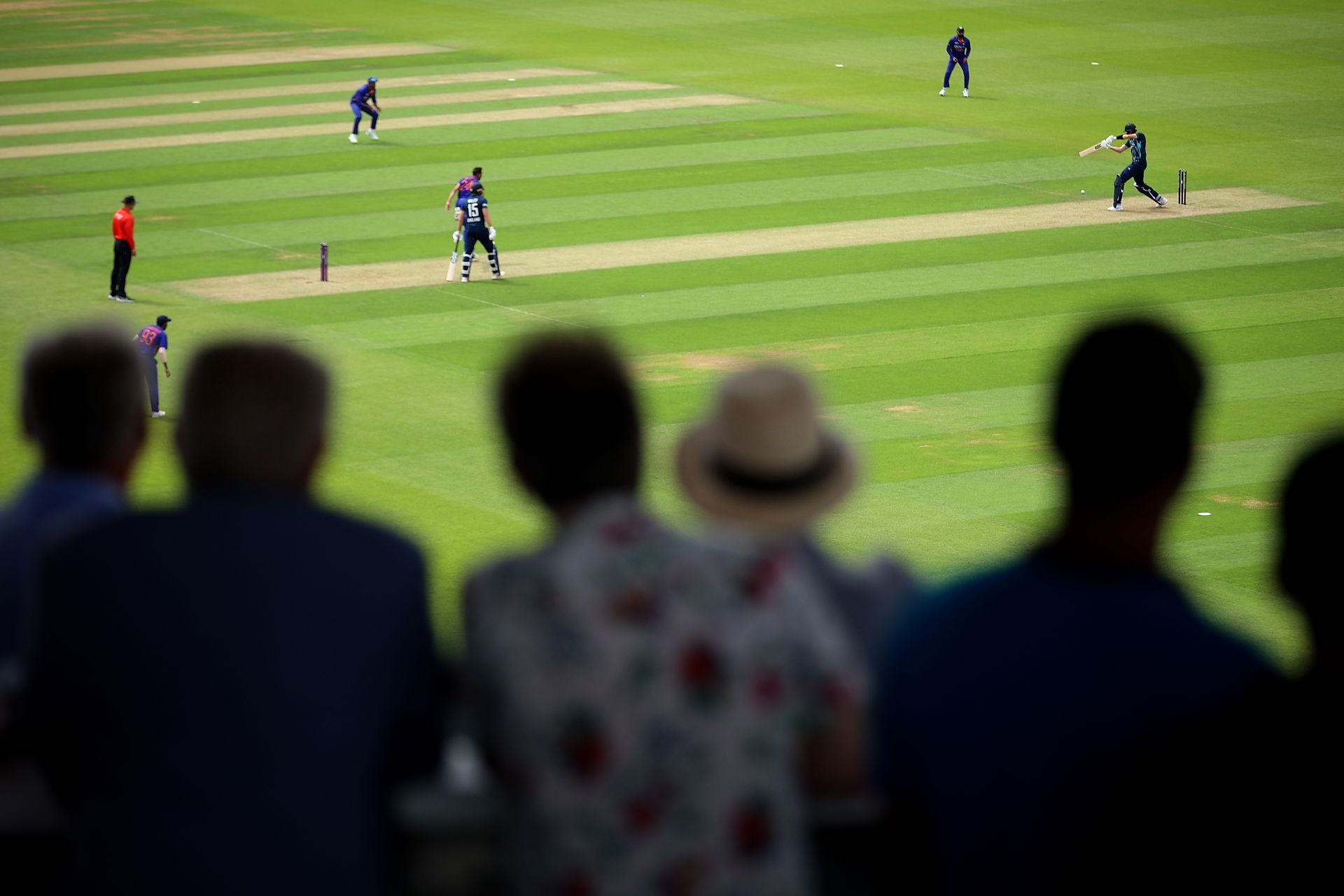 A group of people are watching a cricket match on a field.