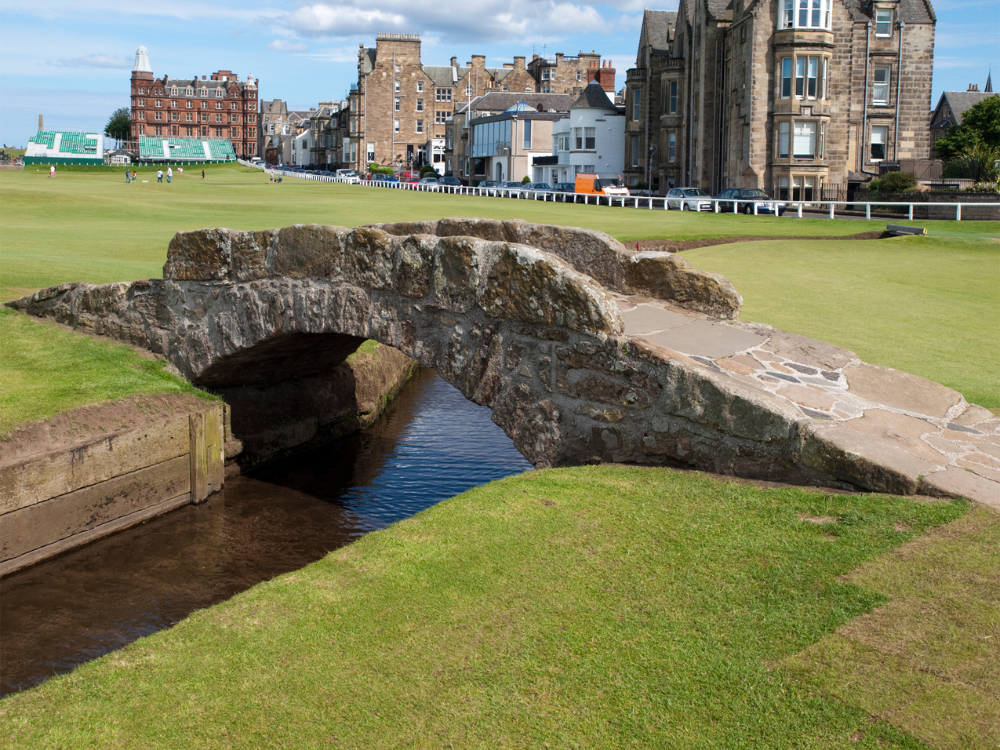 A stone bridge over a stream with buildings in the background