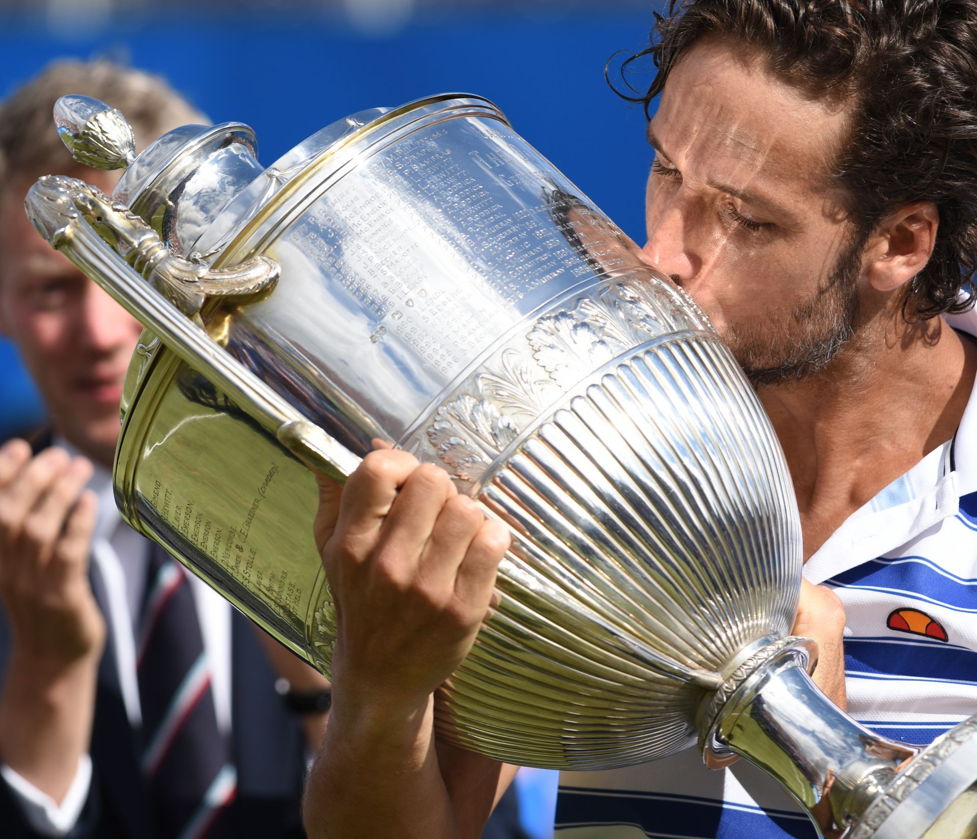 A man in a blue and white striped shirt is kissing a trophy