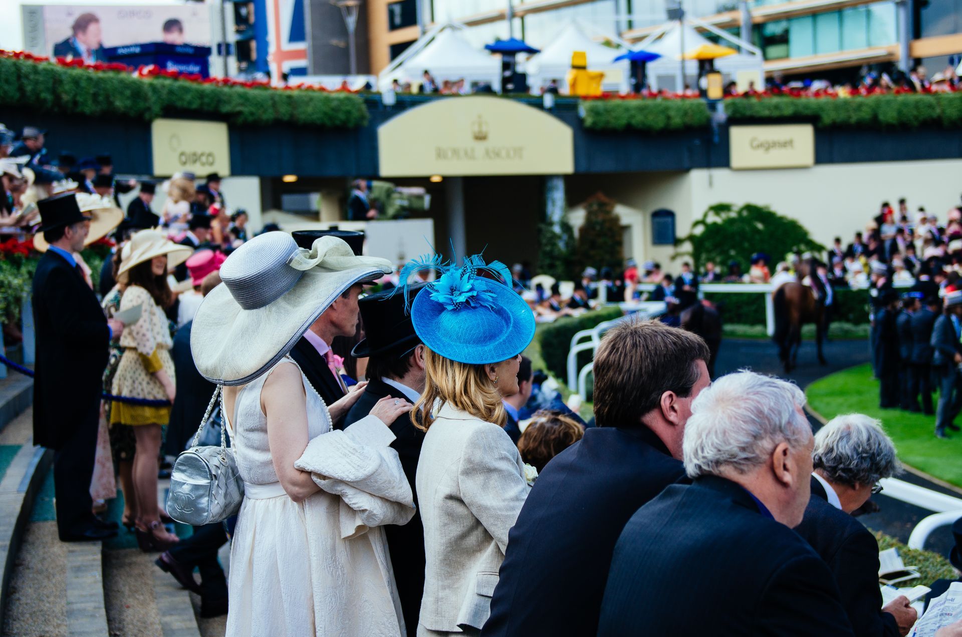 A crowd of people are gathered at a race track wearing hats.