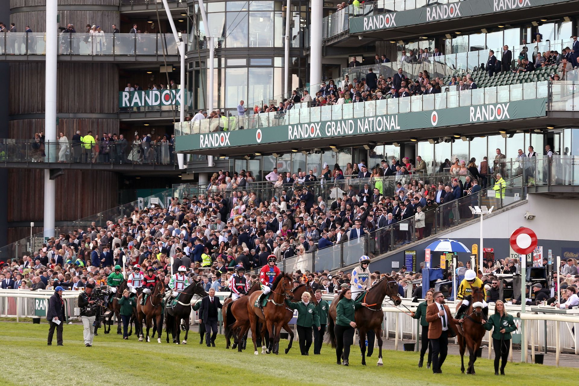 A group of horses are walking in front of a crowd at a race track.