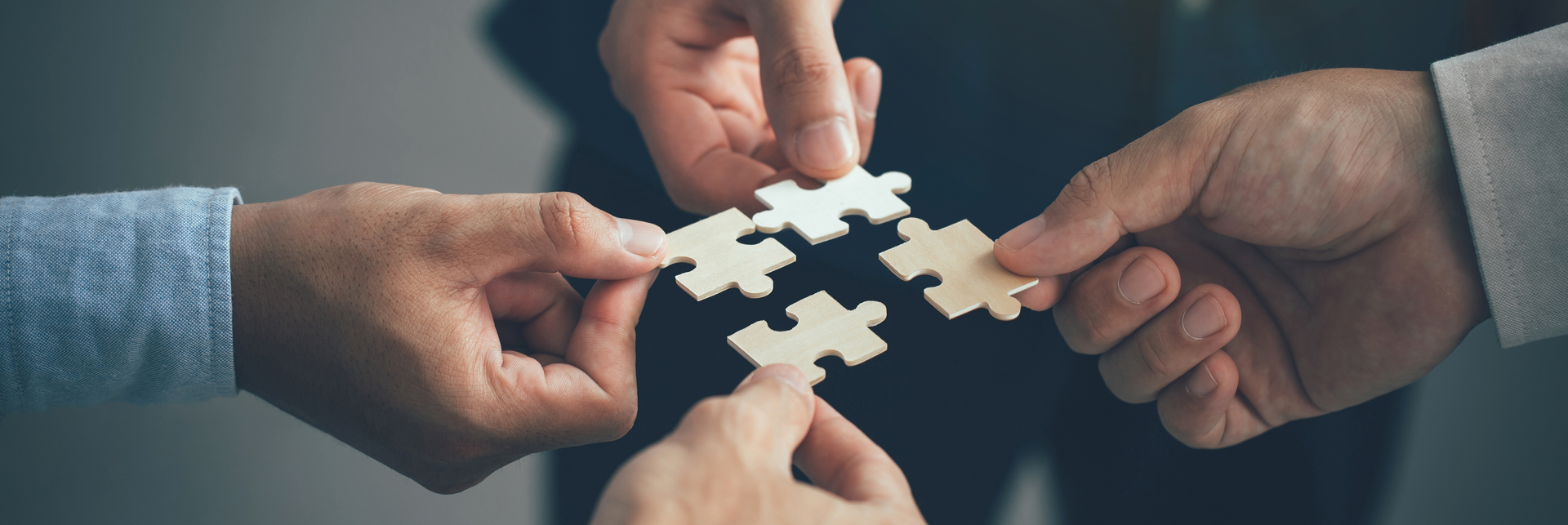 A group of hands collaboratively assembling pieces of a jigsaw puzzle, symbolising teamwork and coordination in planning Corporate Social Responsibility (CSR) events.