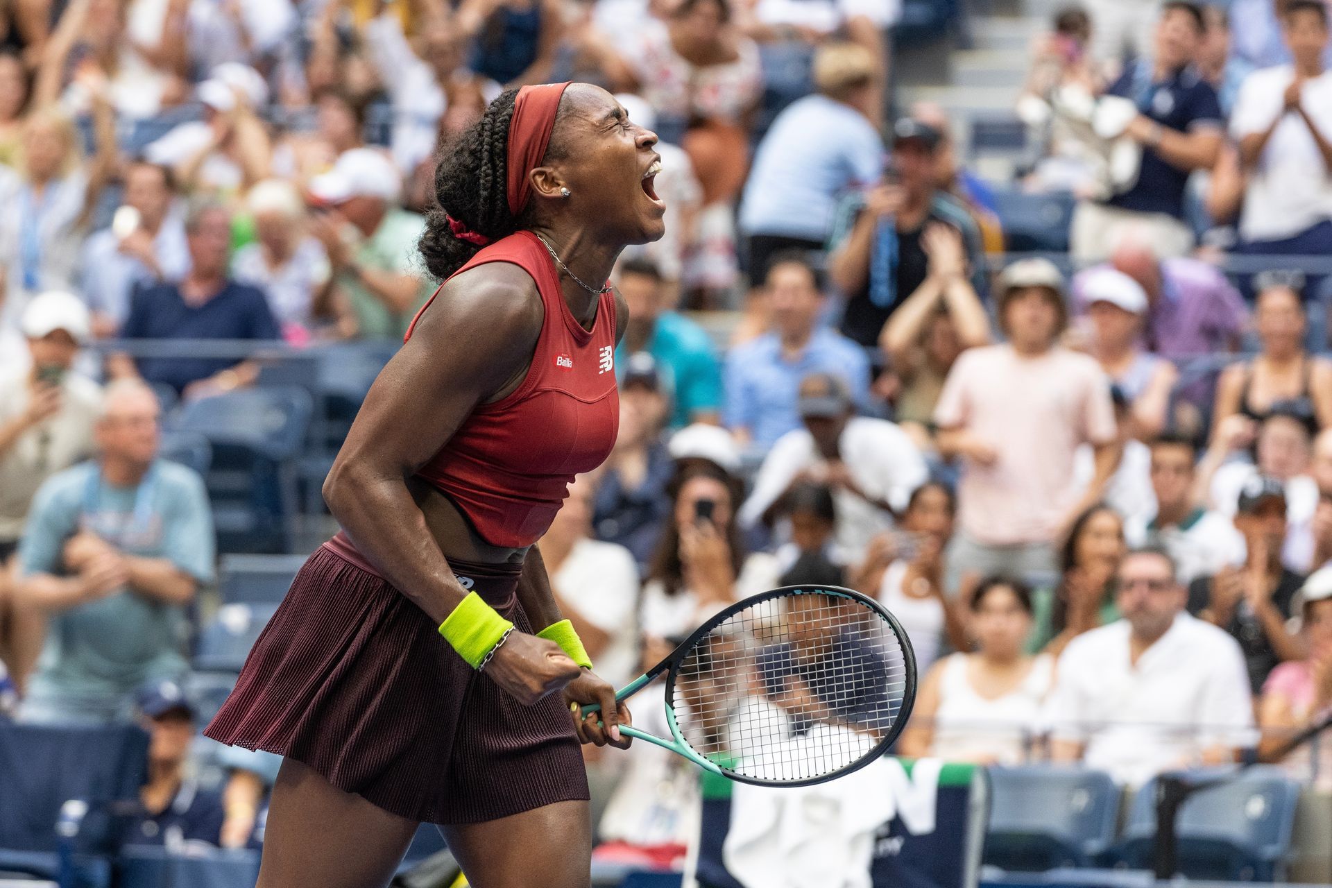 A woman is holding a tennis racquet in front of a crowd.