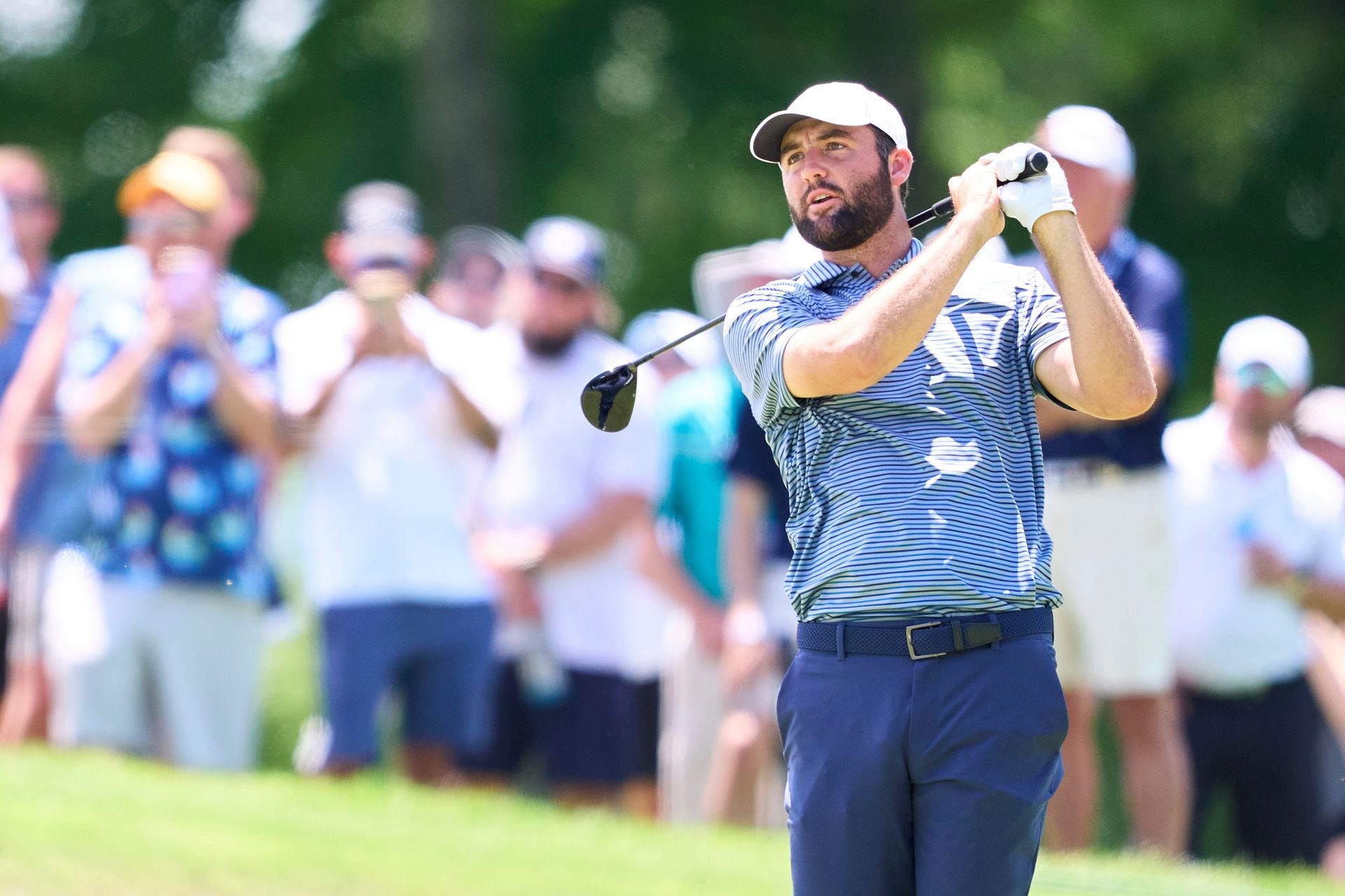 A man with a beard is swinging a golf club on a golf course.