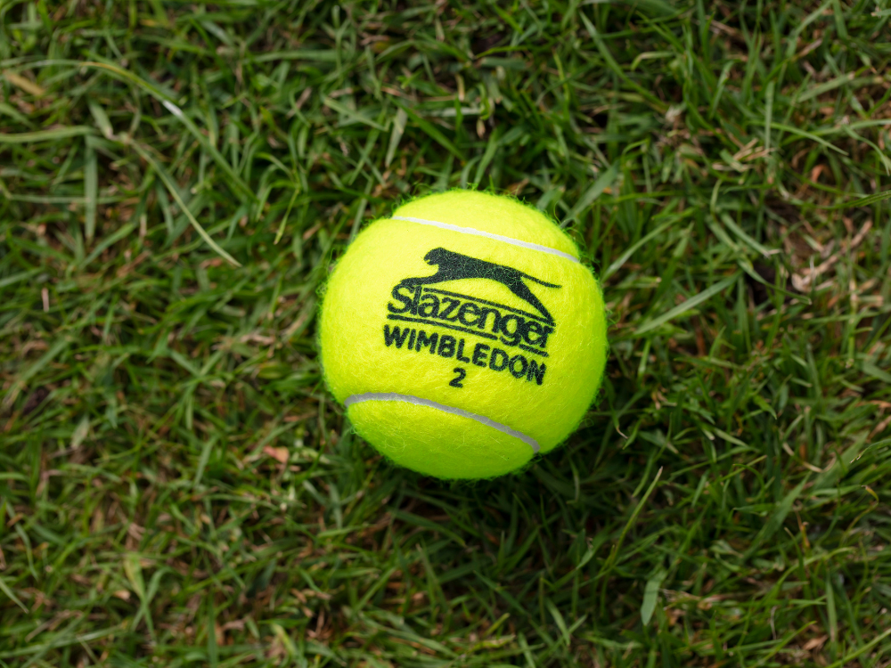 A yellow tennis ball is sitting on top of a lush green field.
