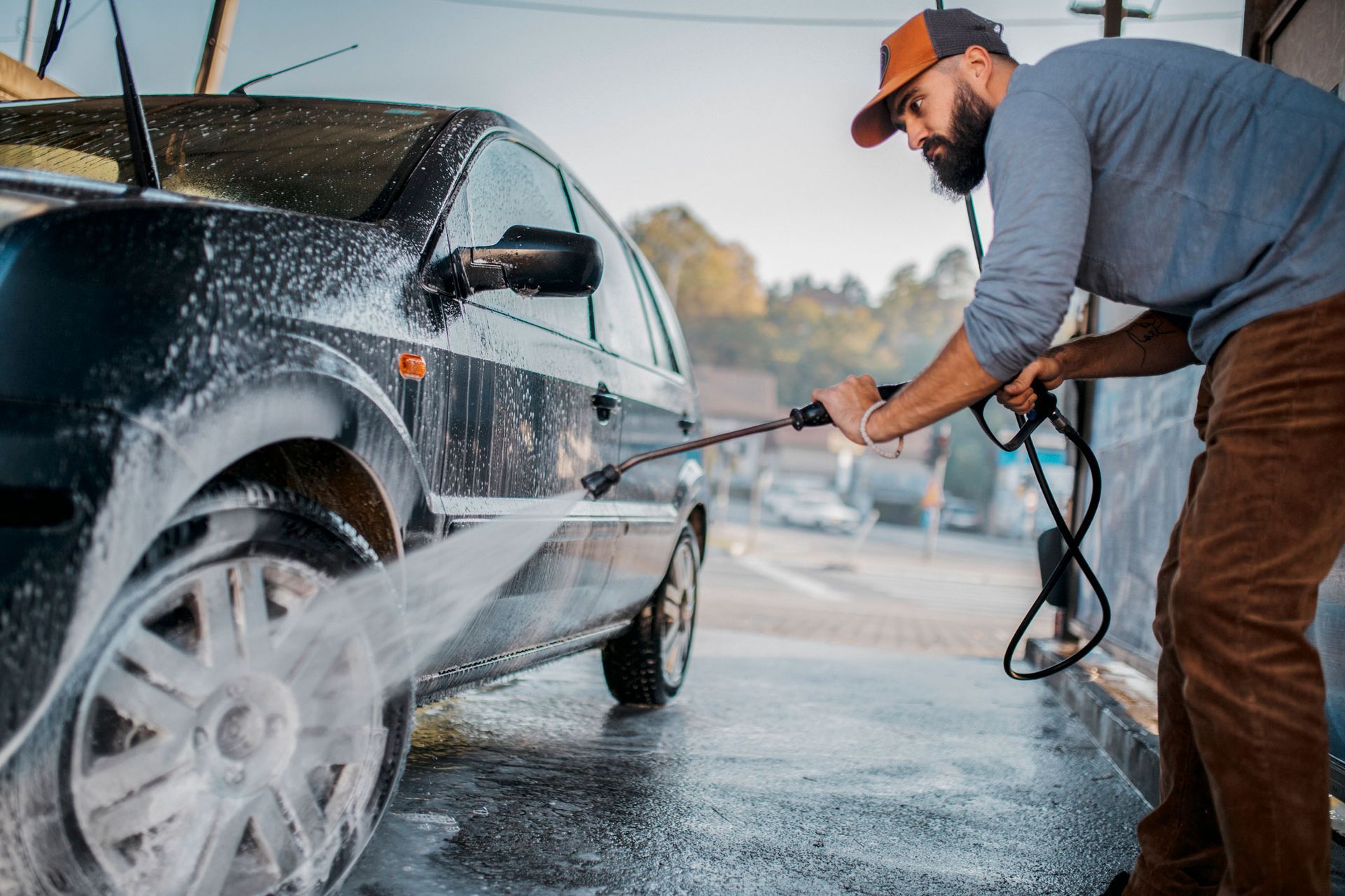 A man is washing his car with a high pressure washer.