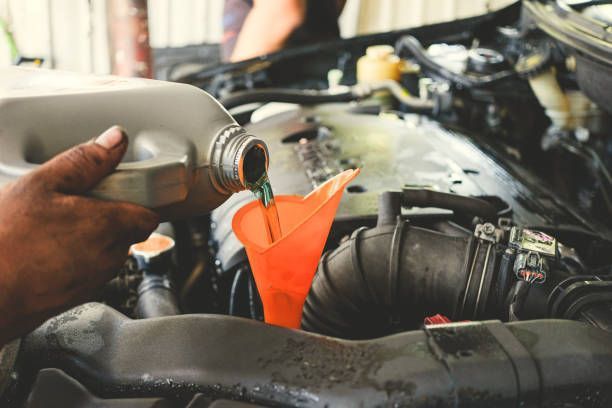 A person is pouring oil into a car through a funnel.