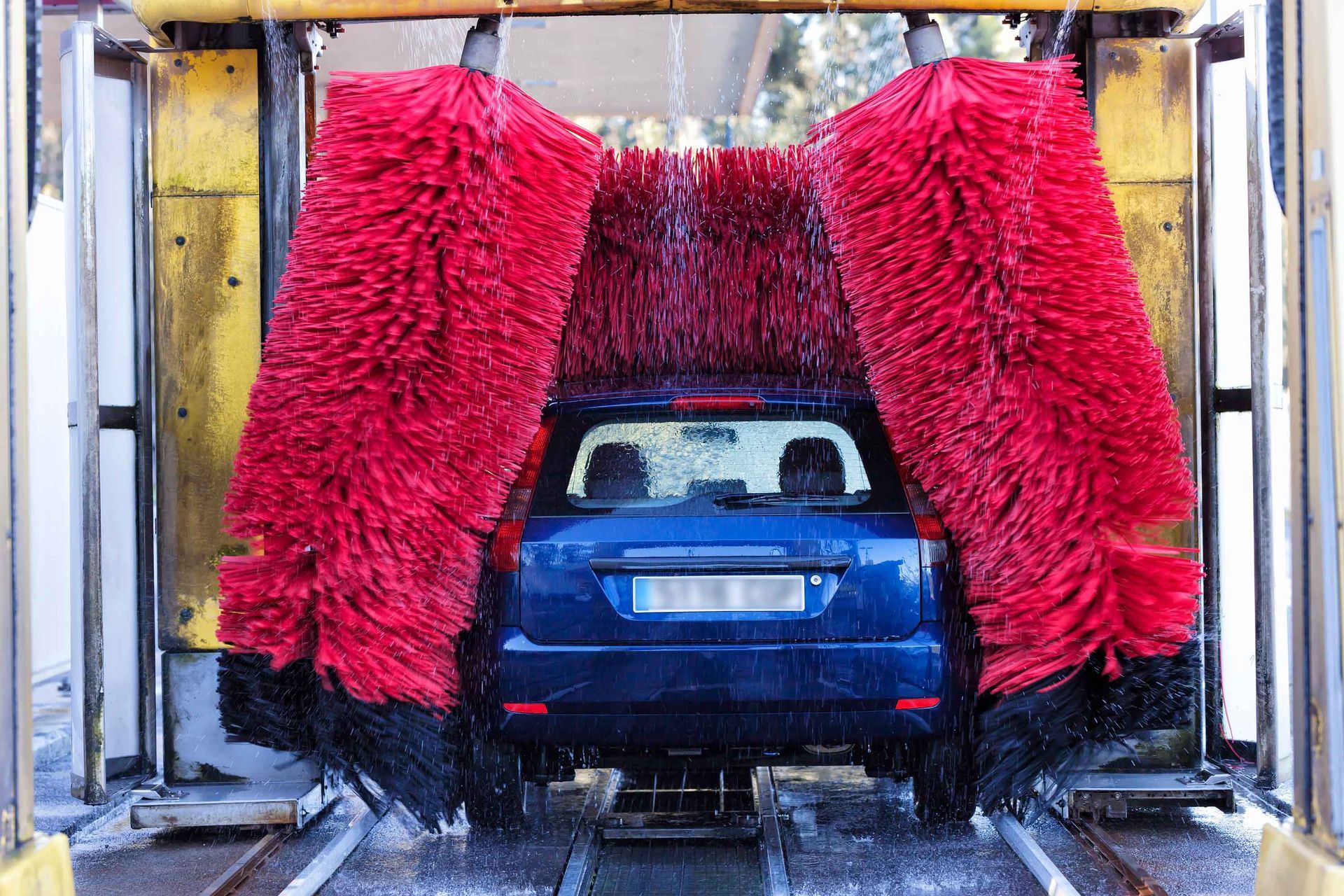 A blue car is going through a car wash with red brushes.