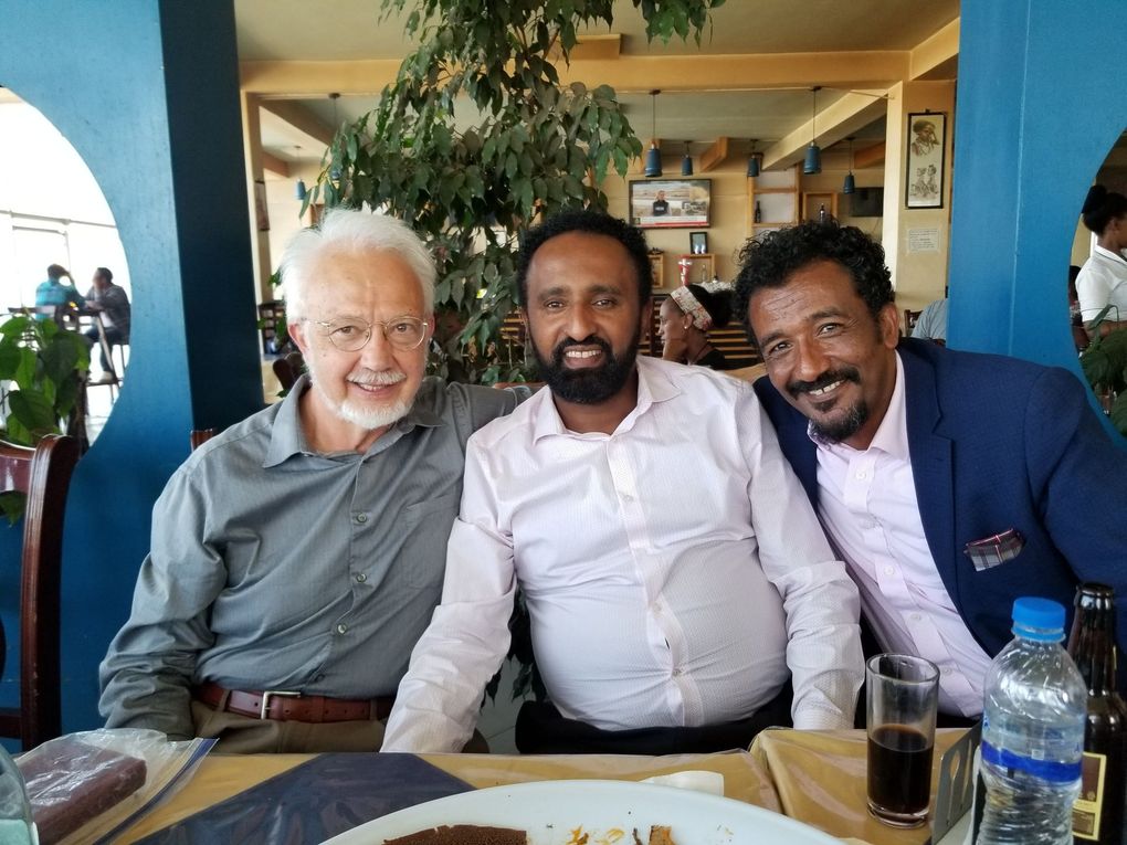 Three men smiling at a table. An older white man, a middle-aged man with a beard, and a man wearing a blue jacket.
