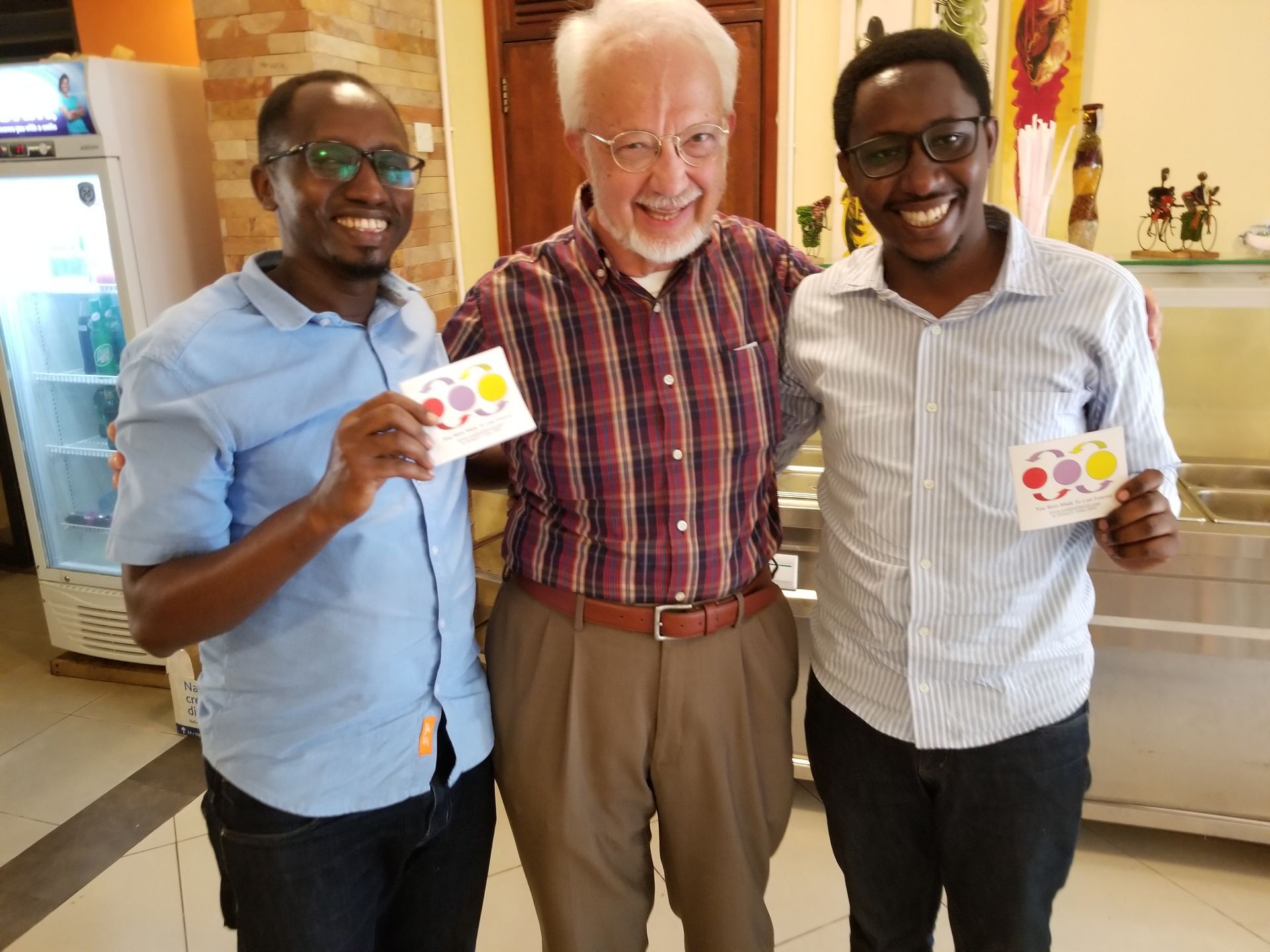 Three men smiling, holding cards. The middle man is older and white, the other two are Black men. Indoor setting.