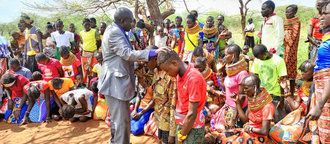 A man in a suit lays hands on a person's head, surrounded by a large group outdoors.