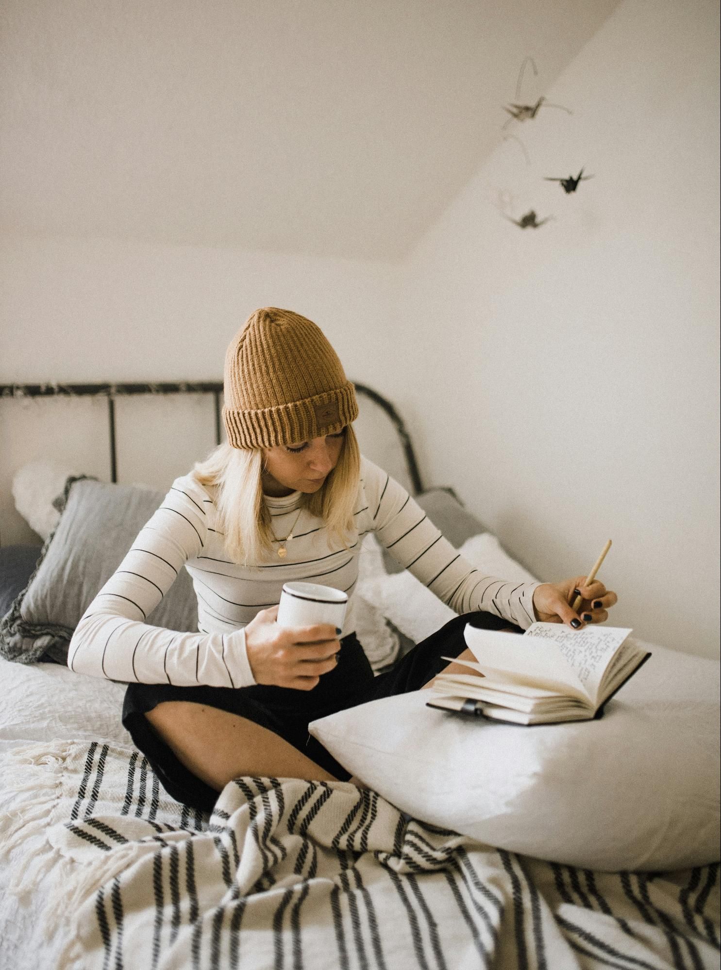 Person journaling on a cozy bed, holding a mug,