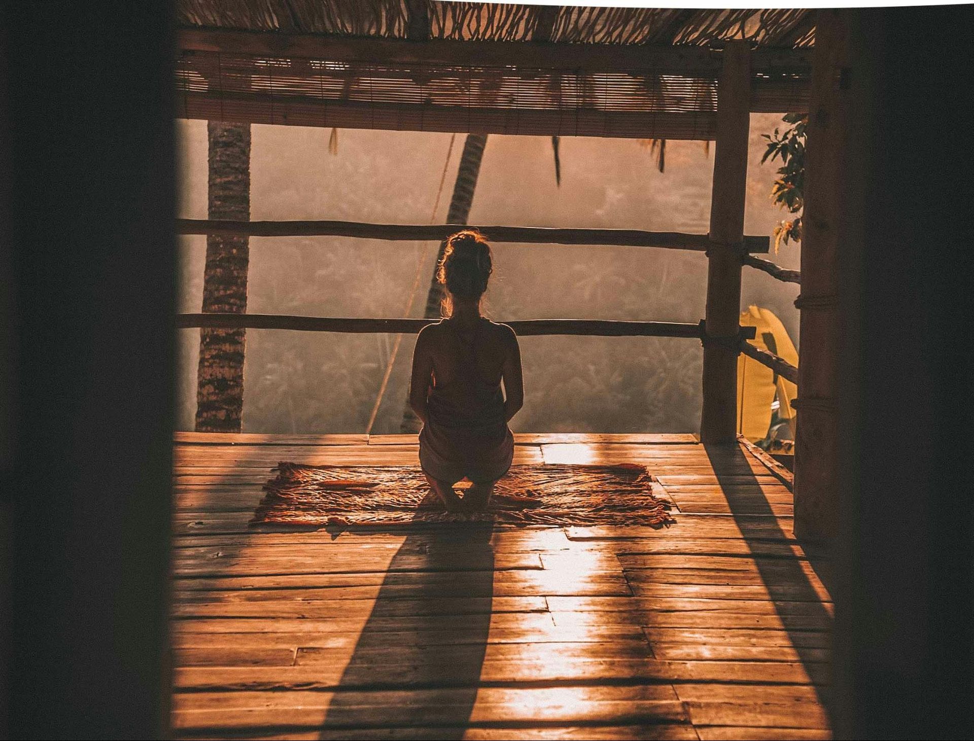 A person sitting on a wooden deck, facing away, meditating in the warm glow of the setting sun.