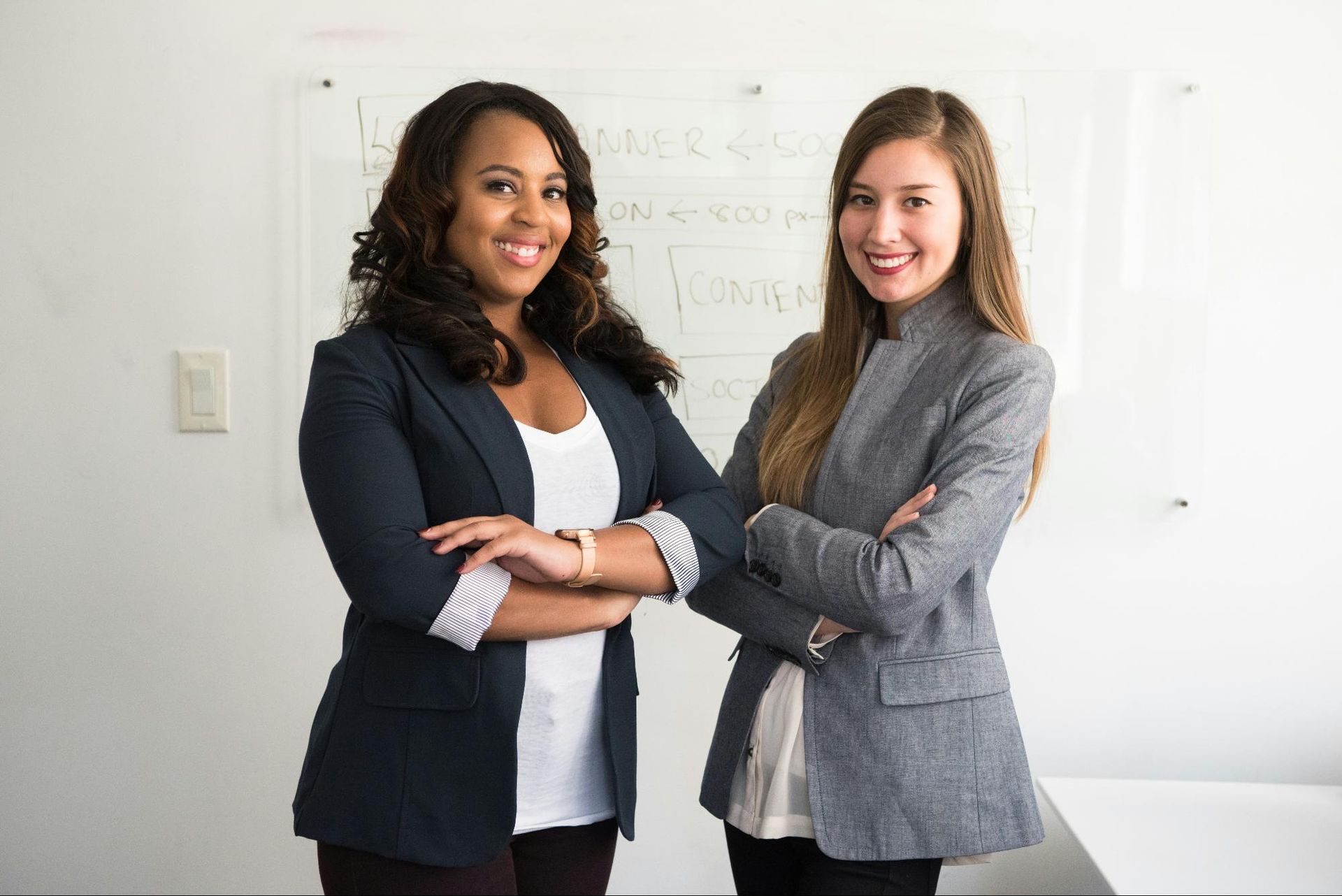 Two smiling professionals standing confidently with arms crossed in an office.