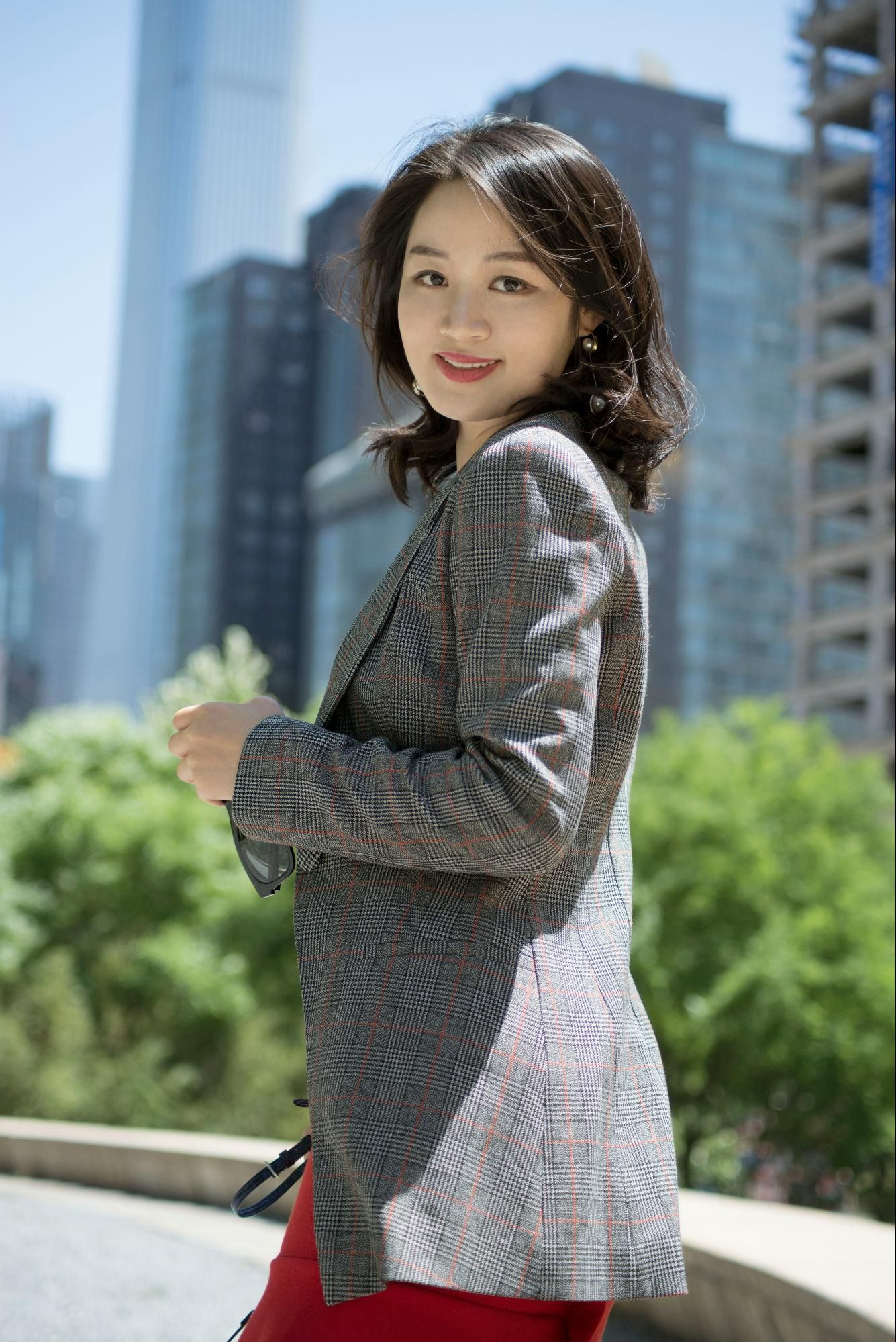 A confident woman in a plaid blazer with a cityscape backdrop.