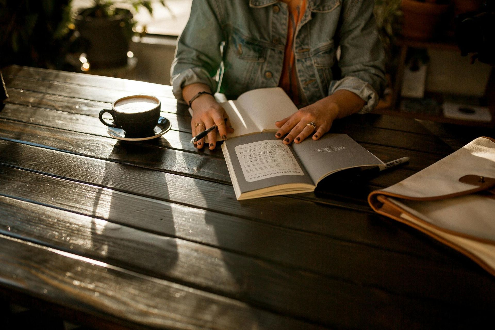 Person reading a book at a sunlit table with a coffee