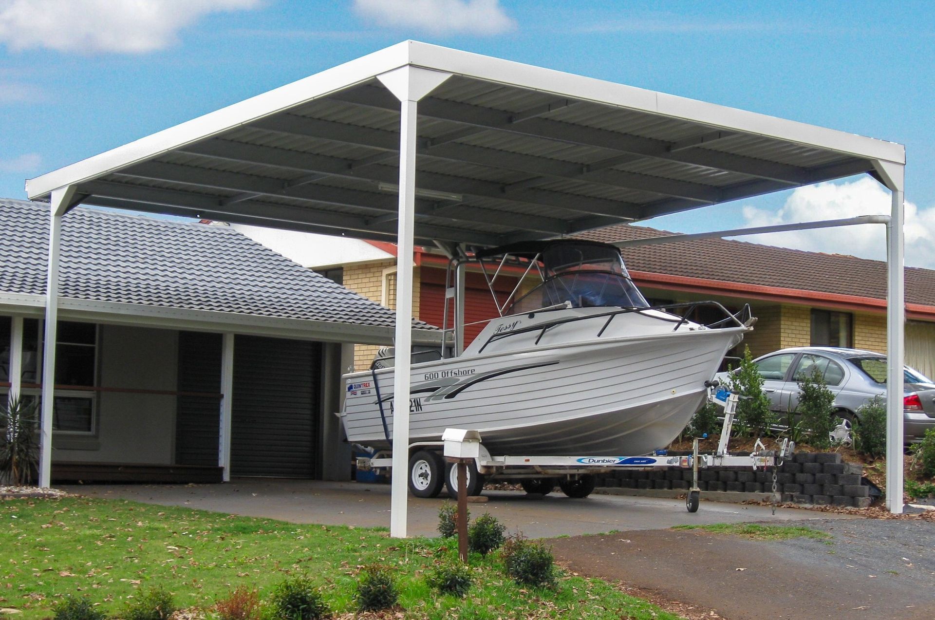 A white boat is parked under a carport in front of a house.