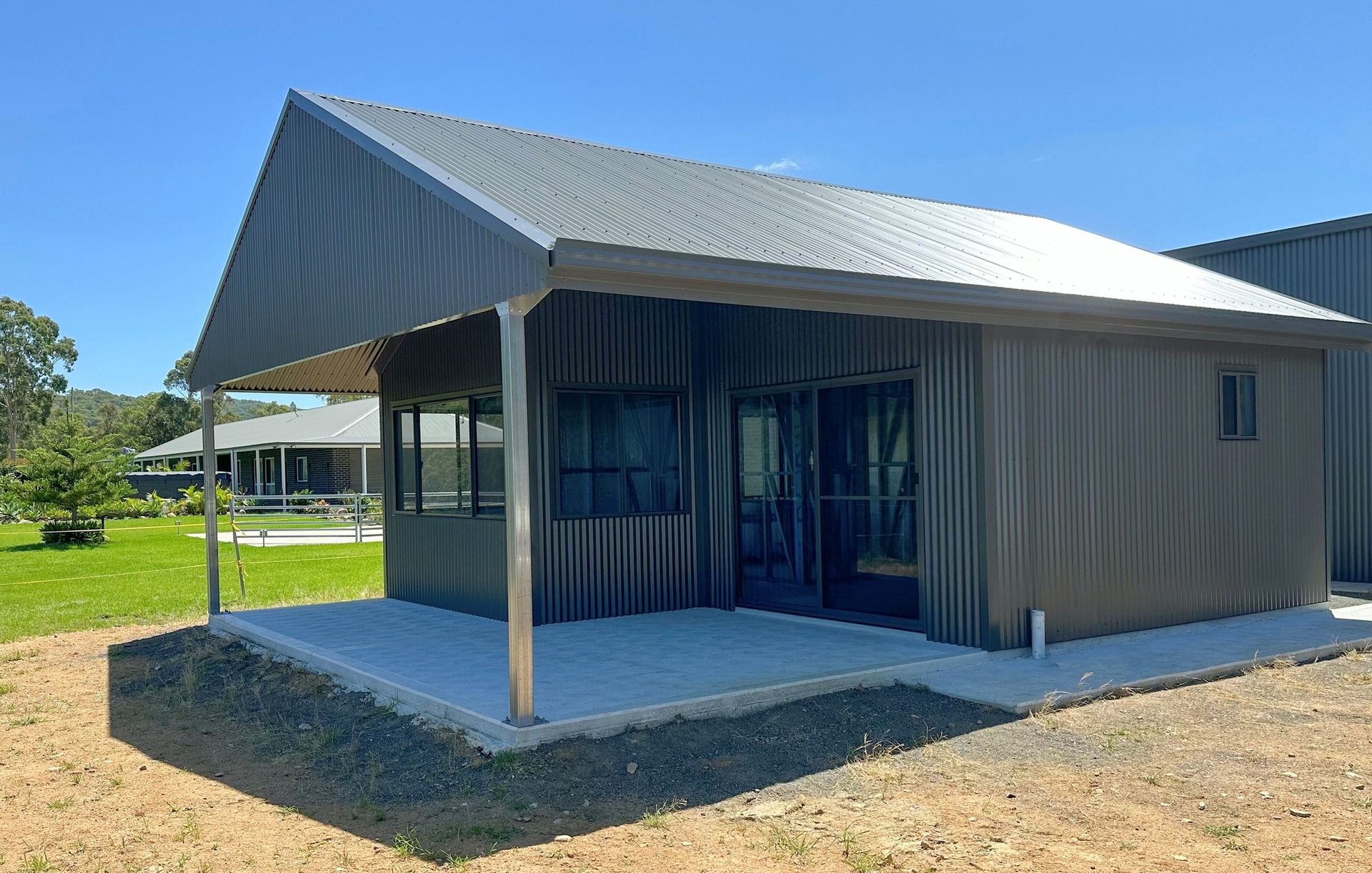 A small house with a porch and a roof is sitting on top of a dirt field.