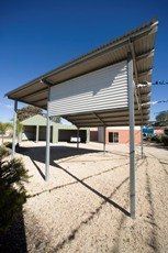 A carport is sitting in the middle of a gravel driveway next to a building.