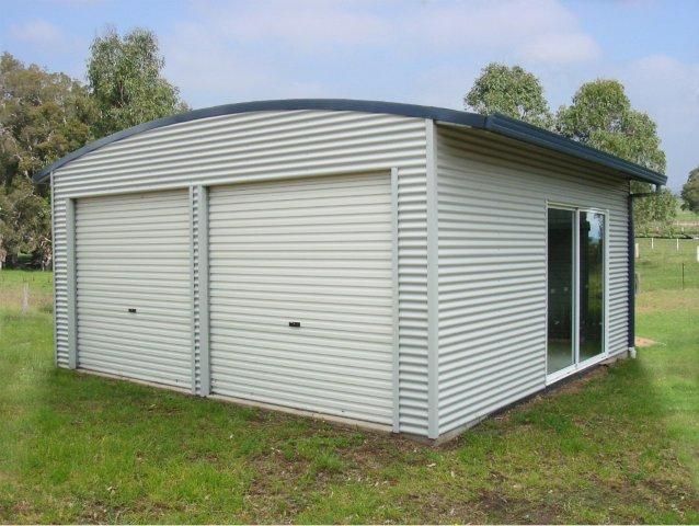 A white garage with a curved roof is sitting in the middle of a grassy field.