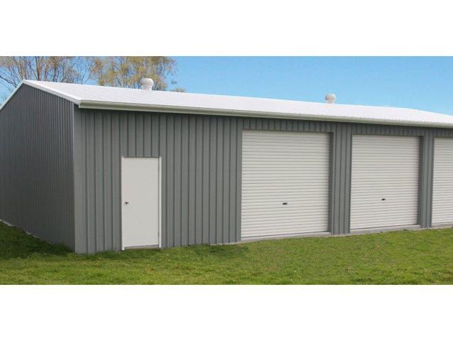 A large metal building with three garage doors and a white roof.