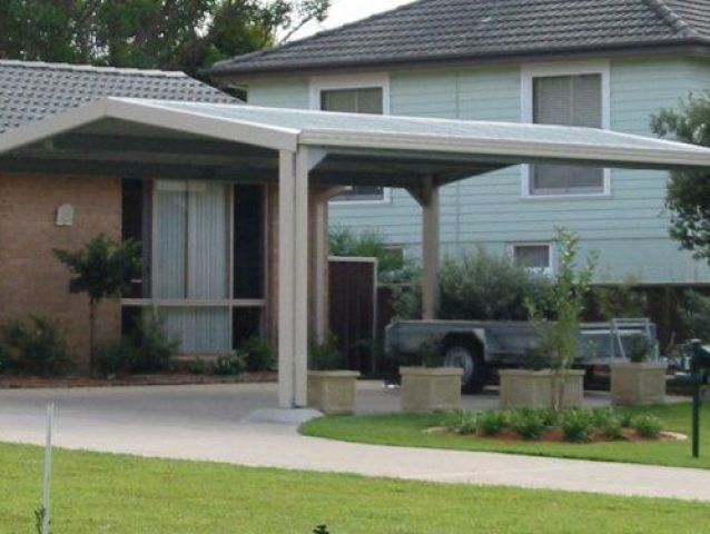A car is parked under a canopy in front of a house