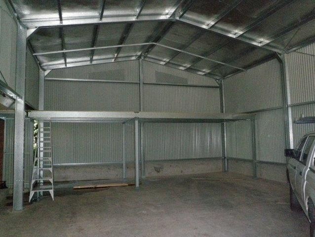 A car is parked inside of a metal building with a ladder.