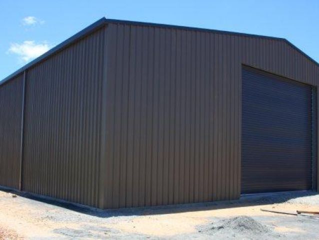 A large brown metal building with a black garage door.