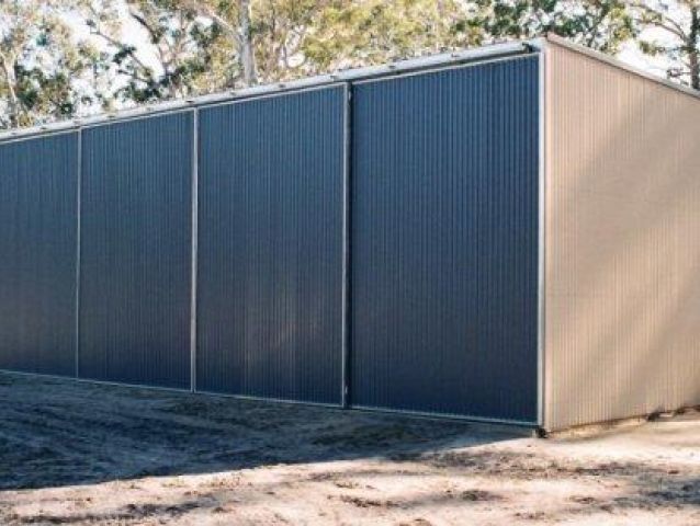 A large shed with sliding doors is sitting in the middle of a dirt field.