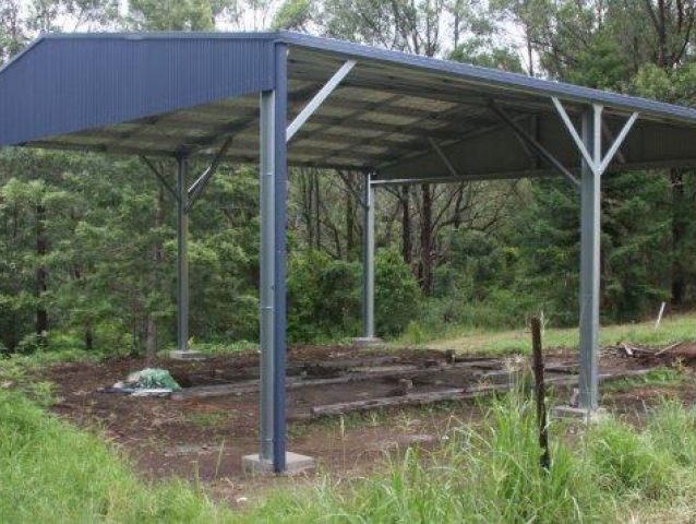 A blue metal shed is sitting in the middle of a grassy field.