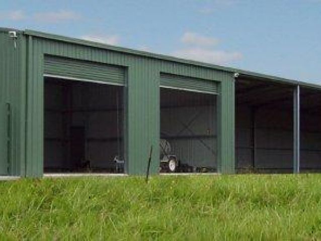 A green building with a lot of doors is sitting in the middle of a grassy field.