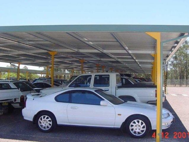 A white car is parked under a canopy in a parking lot