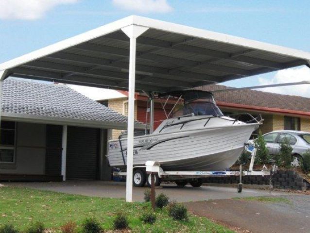 A boat is parked under a carport in front of a house