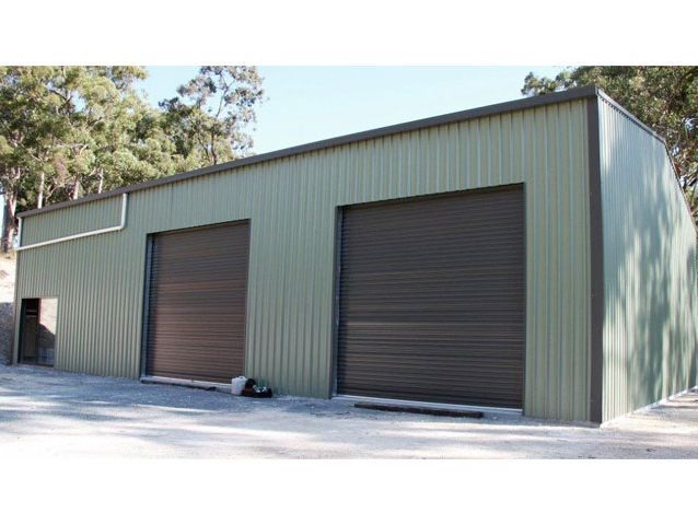 A green metal building with two brown garage doors.
