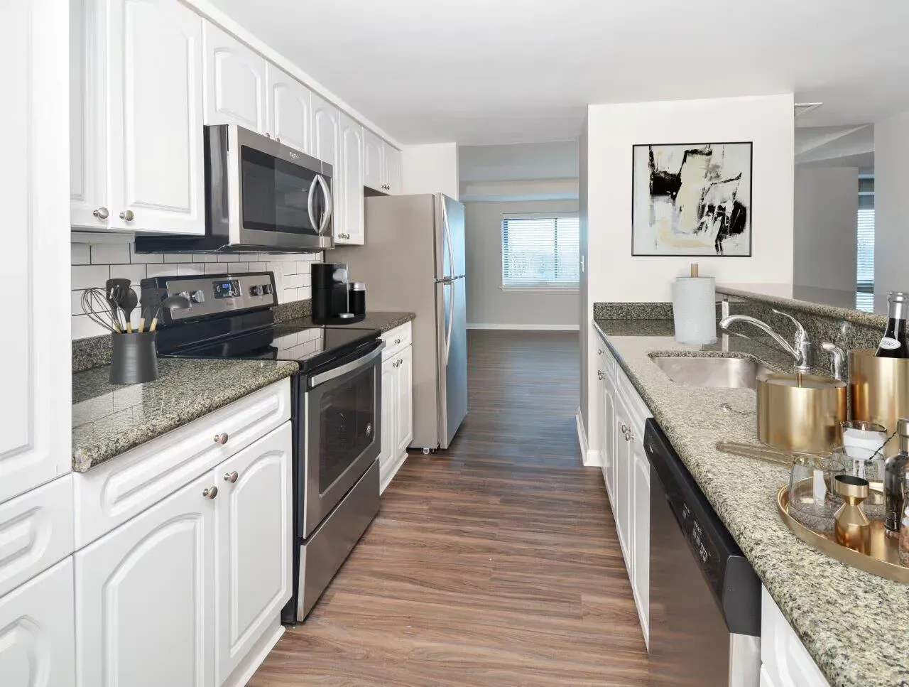 Apartment kitchen with white cabinets, granite counters, stainless steel appliances, and a view of the living area.