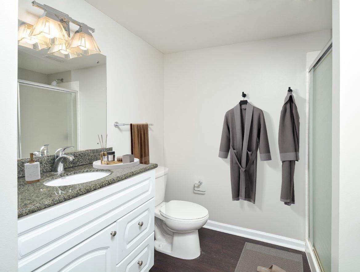 Bathroom with granite countertop, white vanity, toilet, and two gray robes hanging on the wall.