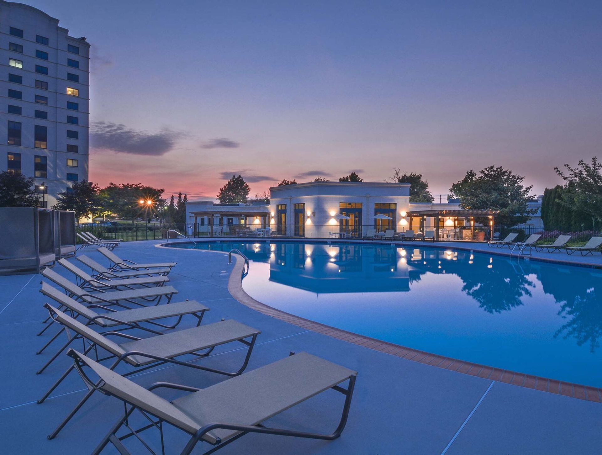 Outdoor apartment community pool at dusk with lounge chairs along the deck.