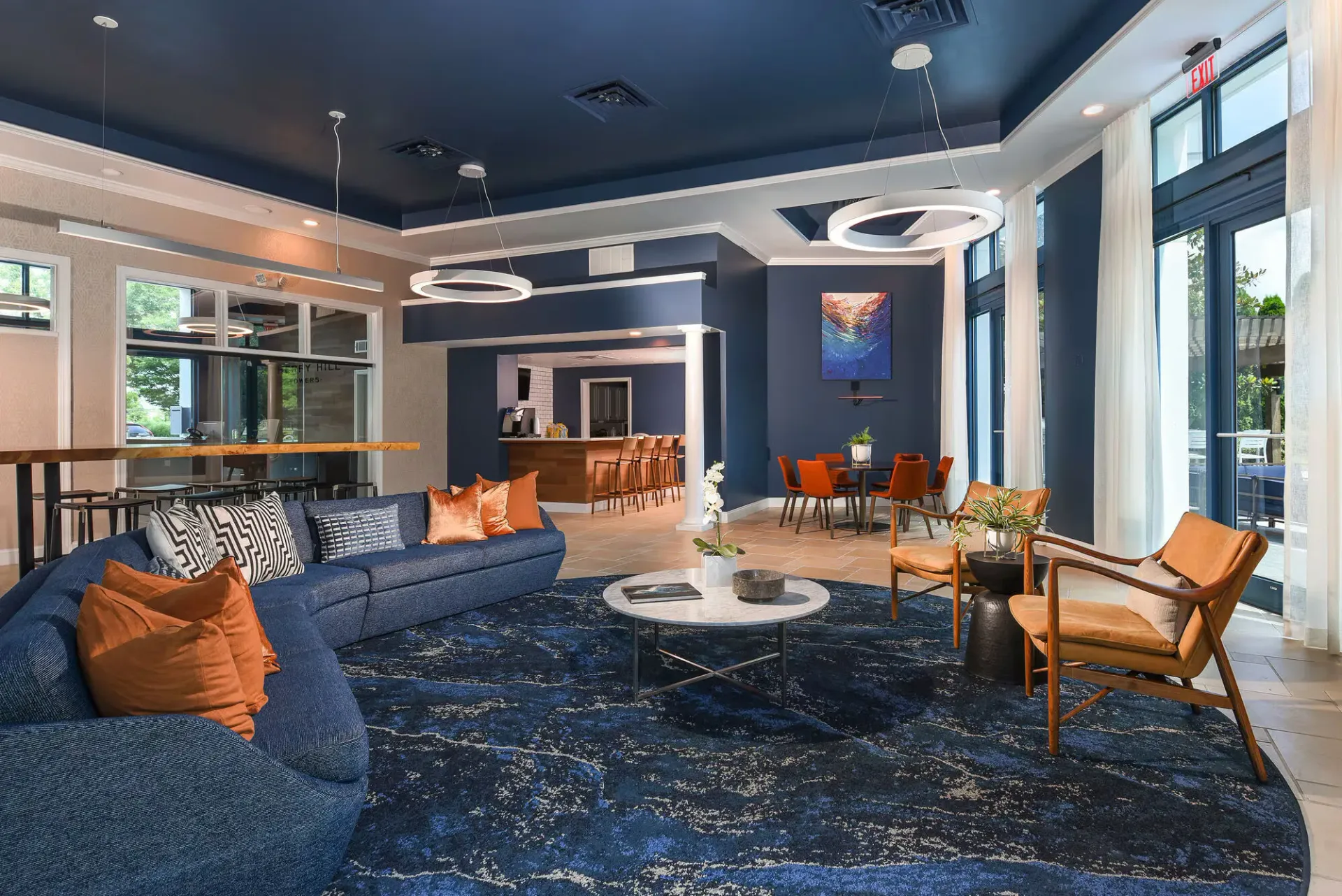 Spacious modern resident lounge with blue walls, circular pendant lights, and comfortable seating.