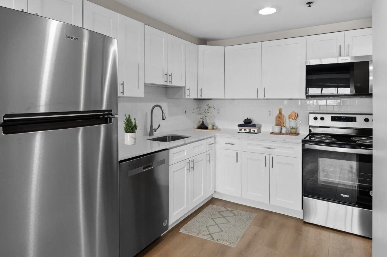 Modern white kitchen with stainless steel fridge, dishwasher, and oven.