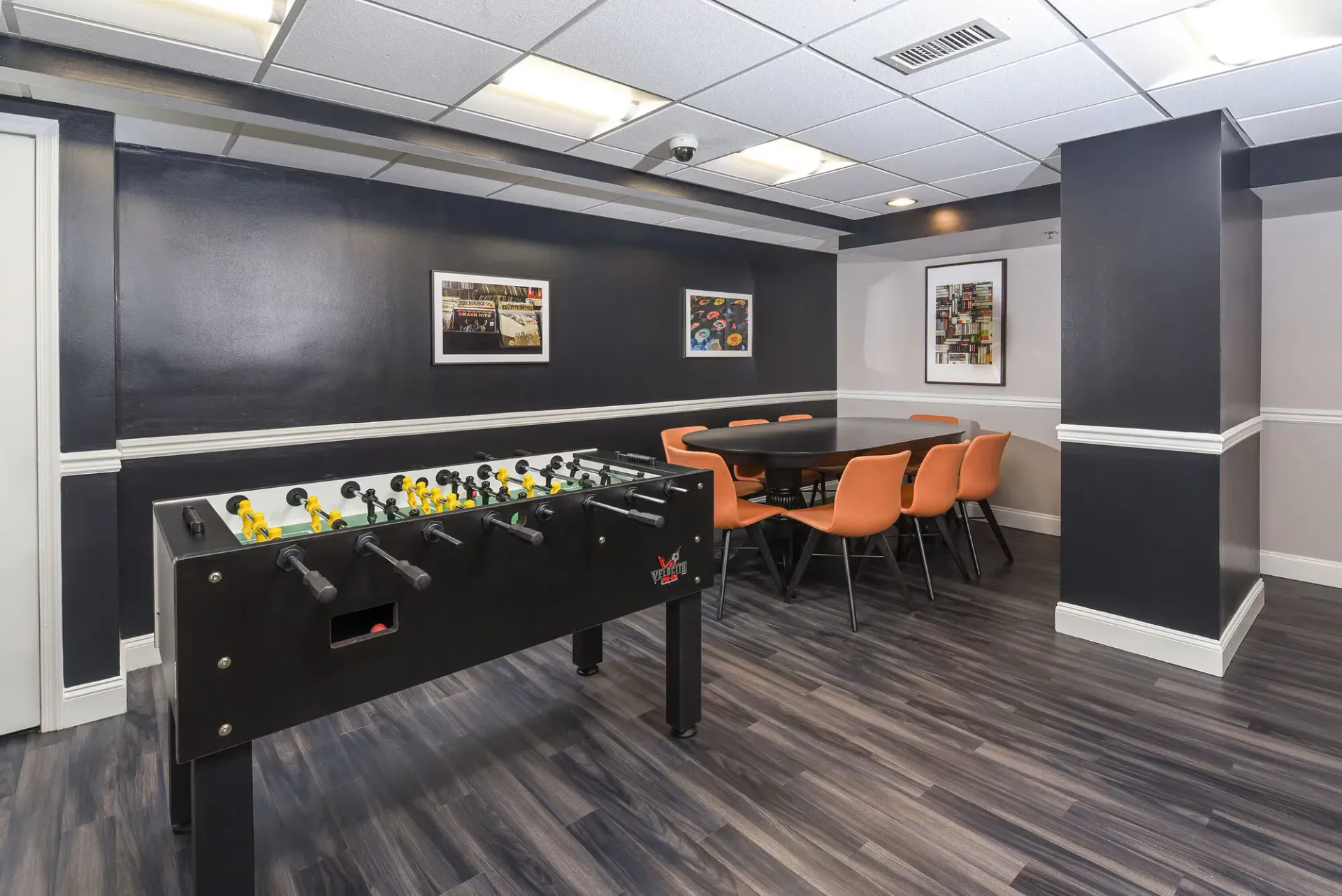 Indoor community recreation room with foosball table and round table with orange chairs.