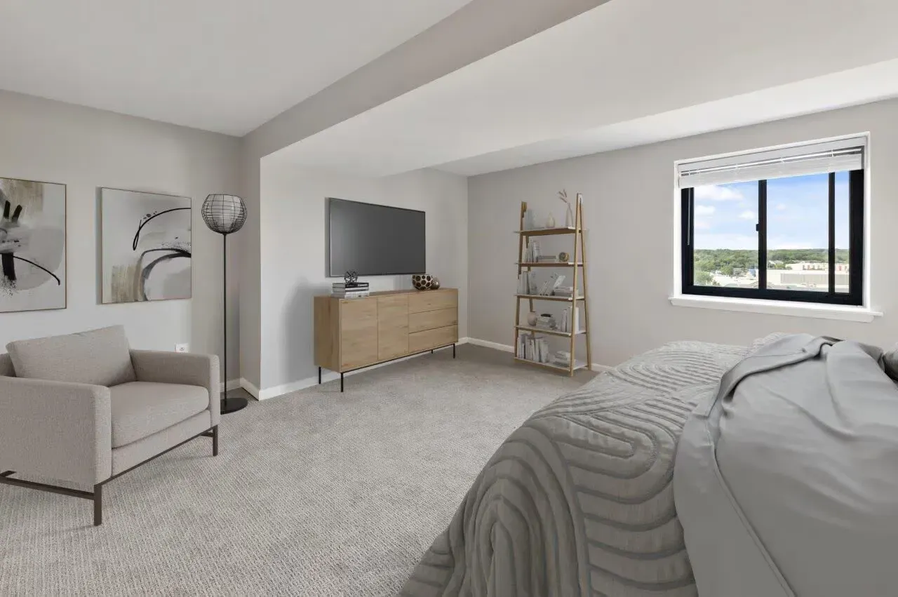Bedroom in a modern apartment with a bed, dresser, bookshelf, and large window.